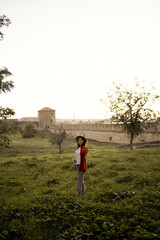 Woman wearing hat standing near ancient fortress in green field