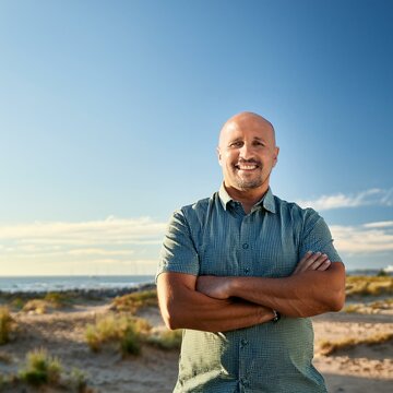 Un hombre calvo, de aproximadamente 40 a&ntilde;os, con una sonrisa amplia y una expresi&oacute;n de confianza. Est&aacute; al aire libre, en un parque verde y soleado, con el cielo azul de fondo.