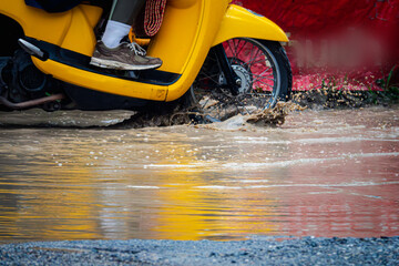A person is riding a yellow scooter through a flooded street. The water is deep and the scooter is splashing water everywhere. The scene is chaotic and dangerous