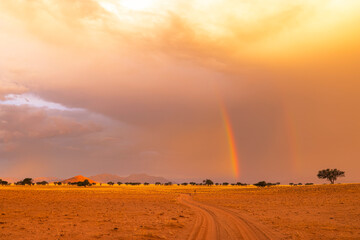 Rainbow and clouds above dry desert sand