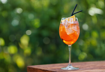 glass of aperol spritz cocktail on table with green natural background