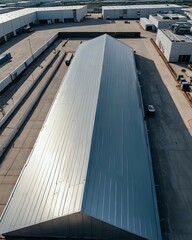 Fototapeta premium Aerial view of a modern industrial warehouse with metal roofing, surrounded by smaller buildings in a clean commercial complex.