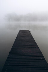 Fototapeta premium Minimalist foggy pier over still water on a misty morning