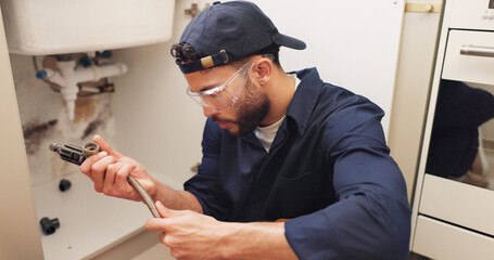 Plumber, man and pipe inspection in kitchen with safety for home maintenance or fixing leak by...
