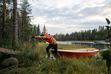 man pulling a boat into a small wooden garage on coast of lake © Cavan