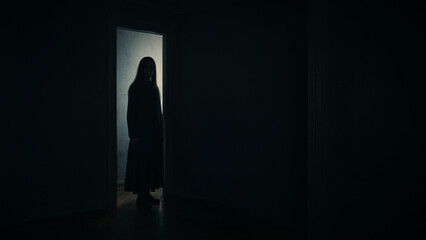 A shadowy woman stood in the corner of the room with a bright open door