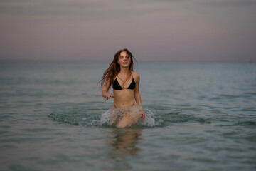 Summer girl running and splashing in sea water. Beautiful sexy woman on the sea. The sexy woman in bikini rest on a tropical beach. Beautiful woman in bikini on the paradise beach.