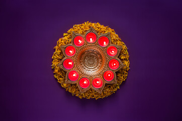 Decorative diya lamps for Diwali festival with orange marigold petals on purple background.