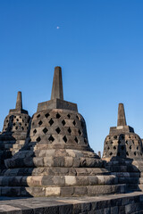Many Stupas on top of Borobudur Temple - an important historical Buddhist monument in Magelang, Indonesia. Moon visible in sky.