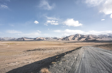 Dusty road of the Pamir Highway winds and twists in the valley of the Tien Shan mountains in Tajikistan in Pamir, landscape in the high desert mountains for background