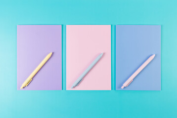 Top view of pink, purple and blue notebooks on blue background. Pink, yellow and blue pens, school, office wallpaper. Flat lay, copy space.