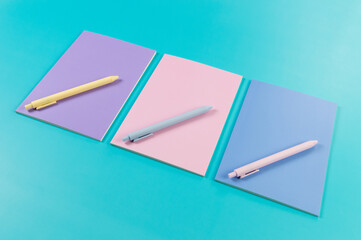 Top view of pink, purple and blue notebooks on blue background. Pink, yellow and blue pens, school, office wallpaper. Flat lay, copy space.