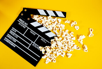Naklejka premium Top view of black and white wooden movie clapperboard with popcorn on a yellow background, concept of film production and entertainment