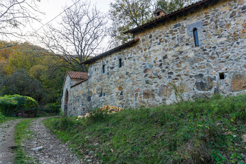 Fototapeta premium A gravel road leads to the outer wall and gate of the monastery. A hill covered with autumn trees is in the background.