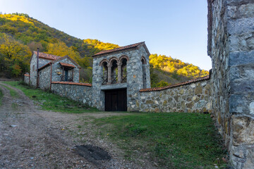 The outer stone wall and bell tower above the monastery gate. A hill covered with autumn trees is...