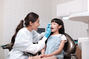 Obraz premium Asian female pediatric dentist checks and examines a little Thai girl's caries teeth in dental clinic, well-being mouth oral hygiene, and professional orthodontic healthcare work in a kid hospital.