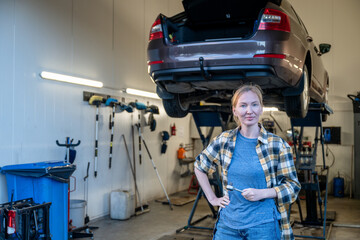 female mechanic holding work tool and standing at entrance of garage