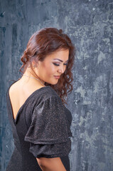Fototapeta premium Sexy girl in black shiny dress with glamorous makeup and wavy long hair posing in studio.