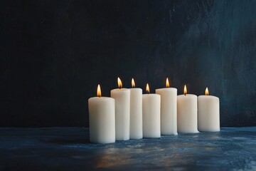 A row of white candles in a dark room, all but one unlit, creating a striking contrast. 