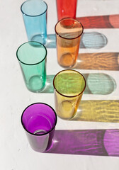 Transparent colorful glasses with sun shadows on harsh light on the white concrete background