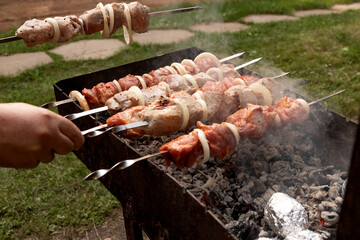 Men's hands cook a juicy, appetizing barbecue on the grill. There are baked potatoes in foil next to it. Barbecue food, proper nutrition, outdoor food, fast food. Family dinner with outdoor barbecue.