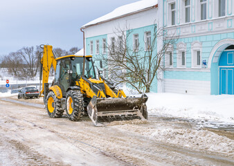 A yellow and black tractor is plowing a snow covered road