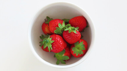 Overhead image of bright red ripe strawberries: multiple fruits in a white bowl