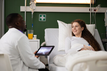 With injury, the patient reclines in the hospital bed as a caring African doctor, holding a tablet with an X-ray, discusses and provides insights into the fracture.