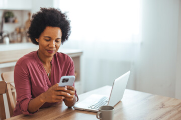 Woman Using Smartphone While Working on Laptop at Home