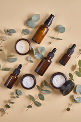 Set of beauty products in amber glass bottles and jars on beige background with eucalyptus leaves. Skin care set for daily routine. Mockup for designers