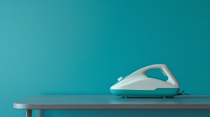 A white and teal handheld vacuum cleaner sits on a gray table against a teal blue wall.