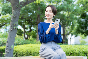 屋外でスマートフォンを操作している若い女性