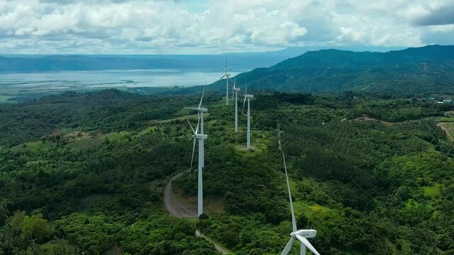 Road along green idyllic landscape of Philippines, Rizal with wind turbines. Rotating propeller of large wind mills on mountain. Pililla Windmills farm in Philippines. Aerial forward wide shot.