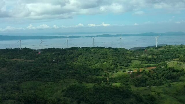 Aerial wide shot showing many wind turbines on coastline of Asian island in Philippines Rizal. Green idyllic landscape with wind turbines in Pililla. Green energy theme.