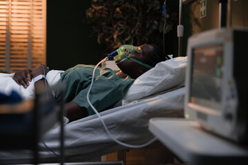 African patient in a hospital bed, utilizing an oxygen mask and monitored by a heart monitor.