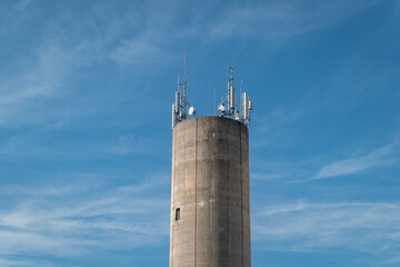 Torre cilíndrica em concreto com algumas antenas que fornecem a cobertura e facilita a comunicação sem fio para dispositivos móveis