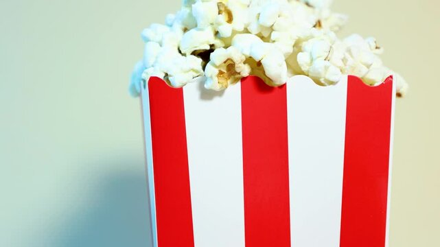 Diagonal close up slow motion of popcorn in red and white cardboard bucket, cinema and popcorn concept