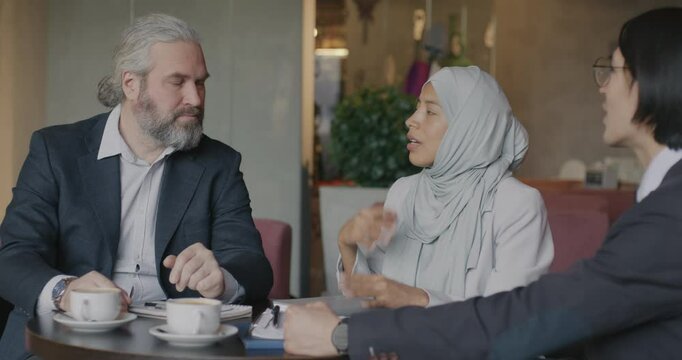 Entrepreneurs talking and shaking hands during business meeting in cafe while female interpreter translating negotiation. Business and cooperation concept.