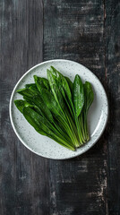 Bunch of fresh green baby spinach leaves on a white plate on a dark wooden background