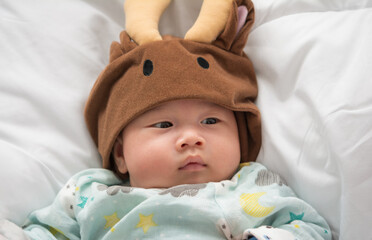 Close-up of male newborn baby wearing hat on his head with relaxed and happy smiling face lying on white bed.