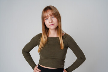 A young woman with straight hair wearing a green top poses against a neutral background