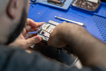 A skilled technician focuses on replacing a phone battery, surrounded by tools and equipment in a vibrant workshop setting
