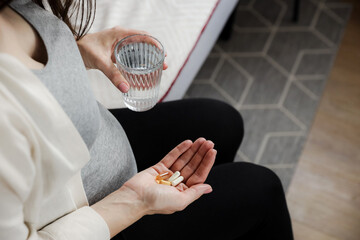 Close up of young pregnant woman holding glass of water and heap of pills in hand, omega 3 in fish...