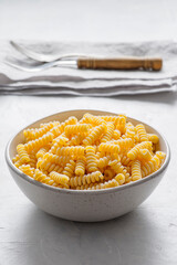 A shiny metal bowl, viewed from the front, is filled with raw pasta 'fusilli'.