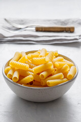 A shiny metal bowl, viewed from the front, is filled with uncooked  pasta 'maccheroni'.