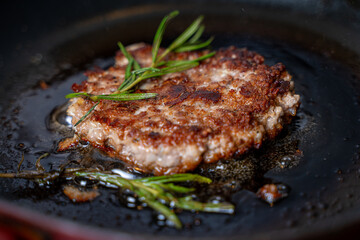 Beef cutlet with rosemary sprigs in a pan. A burger patty is fried on a black background. High quality photo
