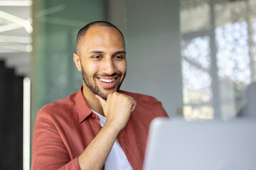 Smiling man wearing casual shirt engaged with laptop, reflecting modern work lifestyle. Person...