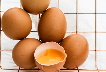 Brown eggs stacked on a metal rack with one broken egg yolk