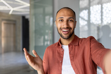 Cheerful man captures selfie on phone during video call in office setting. Expresses joy, connectivity, modern communication, technology use, and friendly interaction.