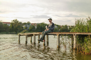 A man sits on a wooden dock, happily holding his dog while overlooking the calm water. The clouds linger above as they relax together in nature.